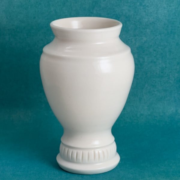 Vase en forme d'urne Vase en porcelaine blanche en forme d'urne, corps ovale posé sur un pied étroit orné de petites lignes verticales, sur fond turquoise.