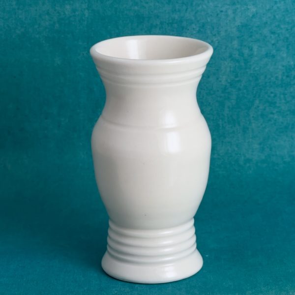Vase classique à anneaux Vase en porcelaine blanche avec un col évasé, un corps arrondi et de fines lignes en relief près du col et du pied, sur fond turquoise.