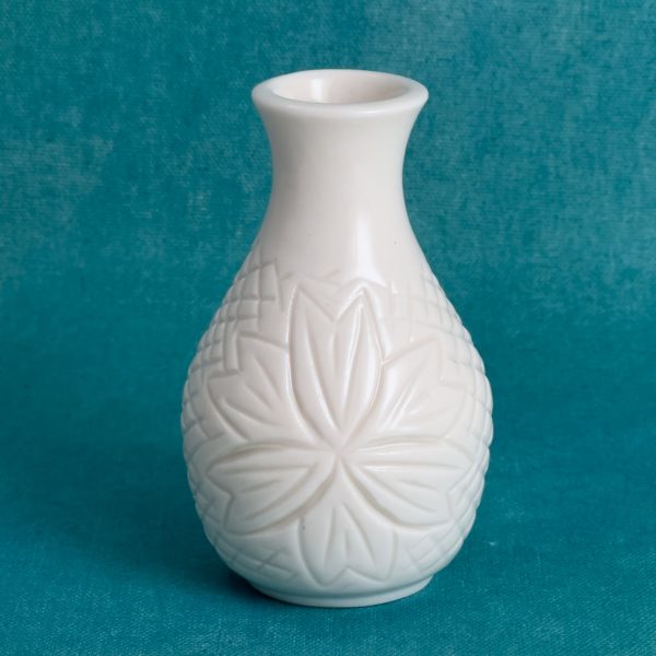Petit vase en porcelaine à col évasé, avec une fleur sculptée entourée d'un motif quadrillé, sur fond turquoise.
