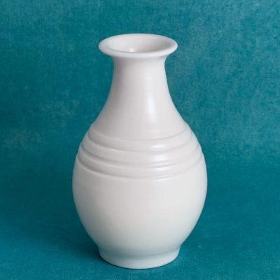 Vase en porcelaine blanche en forme de bouteille, col évasé et panse arrondie, marqué de fines rainures à l'épaule, sur fond turquoise.