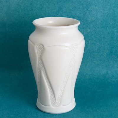 Vase facetté à motif texturé Vase en porcelaine blanche à panneaux facettés, orné d'un motif en relief texturé sur le devant, sur fond turquoise.