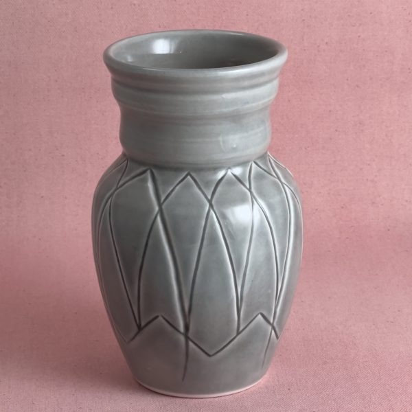 Vase gris à losanges Vase en porcelaine grise au col cerclé, dont la panse est gravée d'un réseau de losanges formant un zigzag continu, photographié sur fond de lin rose.