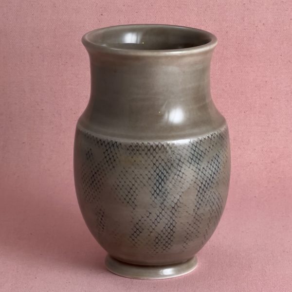 Vase en porcelaine grise au col évasé et à la base texturée d'un motif en losanges, sur fond de tissu rose.