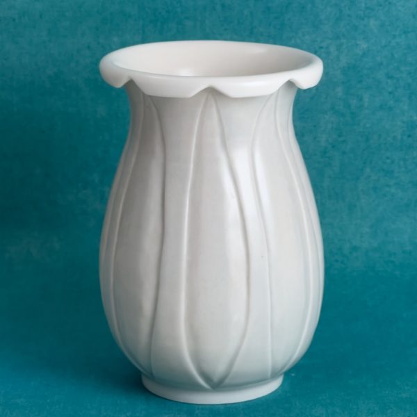 Vase en porcelaine avec des lignes verticales en relief sur tout le corps et un bord ondulé comme des pétales, gris très pâle à l'extérieur et blanc à l'intérieur, sur fond turquoise.